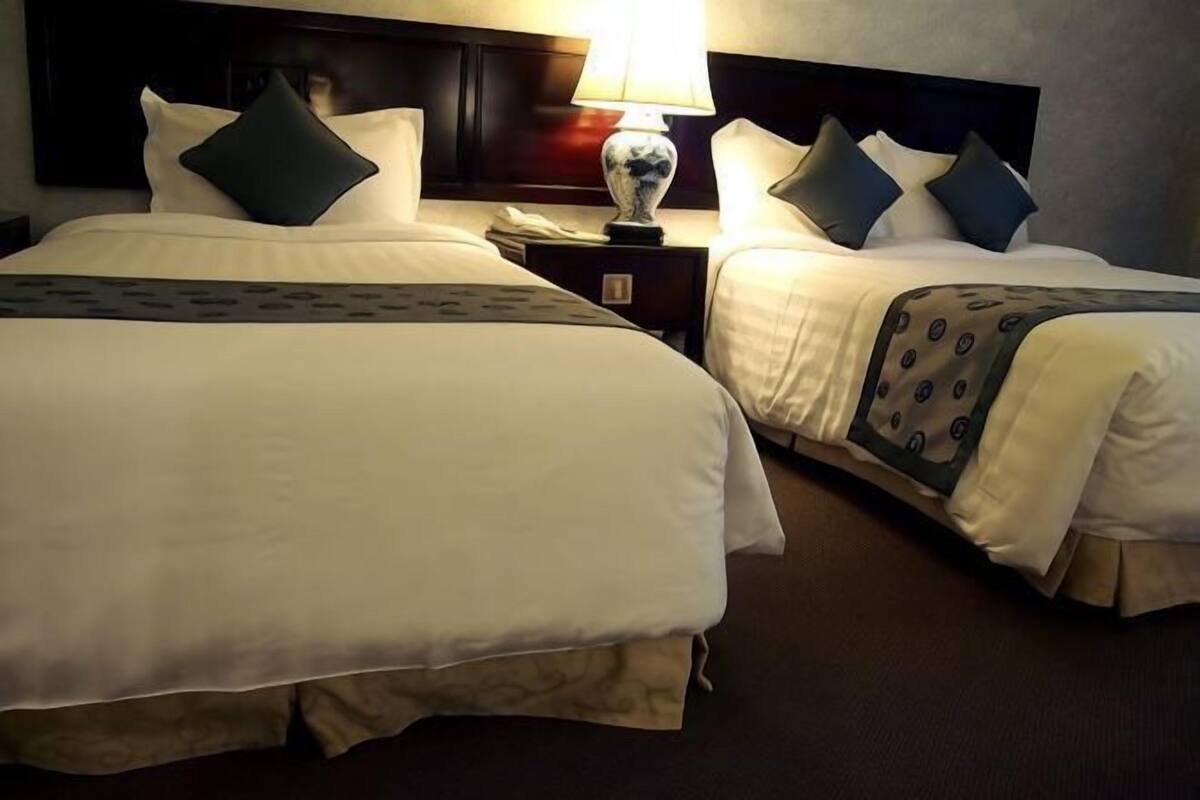 Two adjacent hotel beds with white linens, dark headboards, and matching throw pillows.