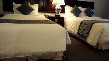 Two adjacent hotel beds with white linens, dark headboards, and matching throw pillows.