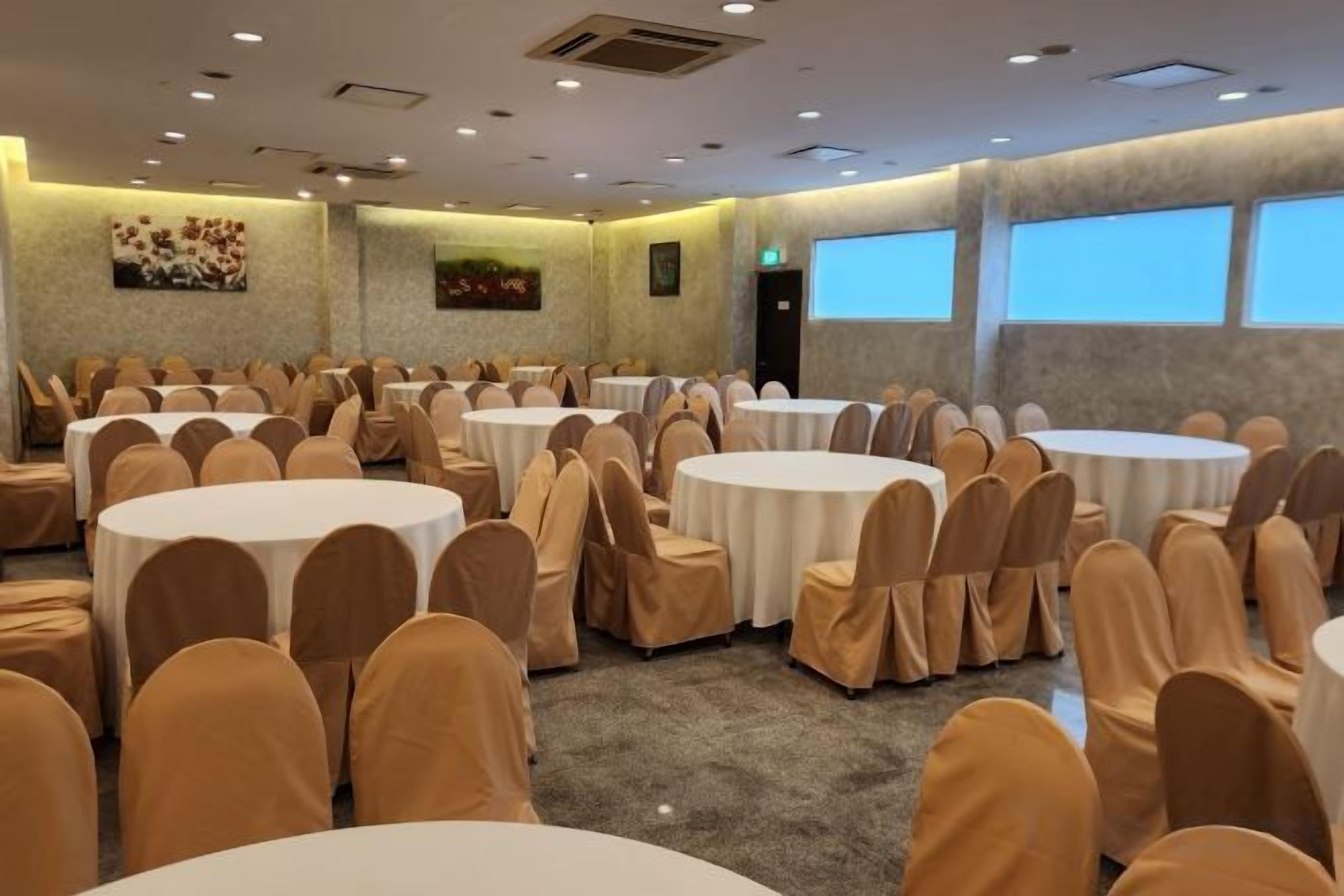 Un salón de conferencias con varias mesas redondas y sillas, ventanas amplias y obras de arte en las paredes.