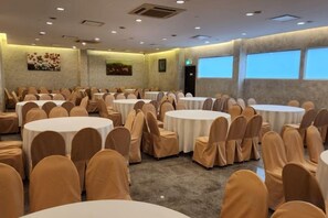 Un salón de conferencias con varias mesas redondas y sillas, ventanas amplias y obras de arte en las paredes.