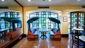 A restaurant with a central table surrounded by booths, large windows with colorful panes, and a polished floor. - Hotel Royal Singapore (Singapore)