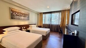 A hotel room with two beds, a TV, a painting, and a large window with curtains. - Hotel Royal Singapore (Singapore)