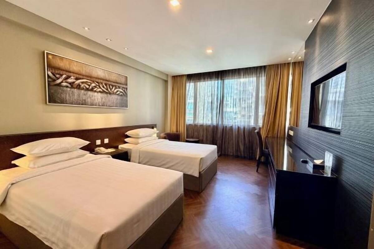 A hotel room with two beds, a TV, a painting, and a large window with curtains.