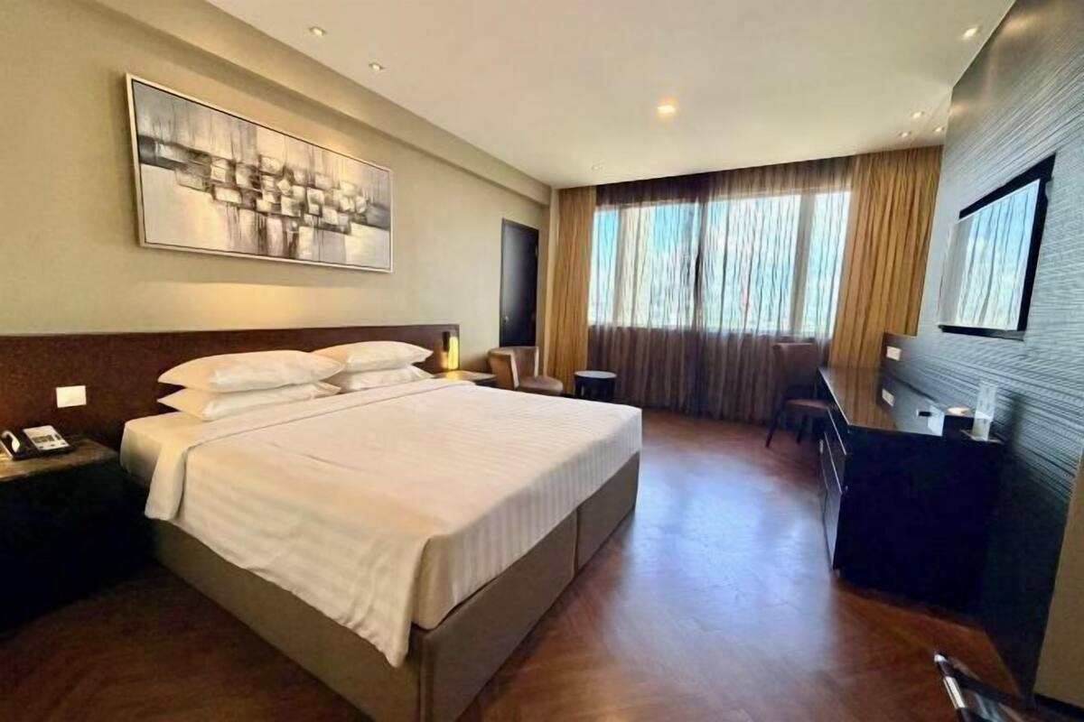 A hotel room with a large bed, a desk, a chair, a TV, and a painting on the wall.