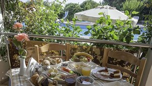 A table set with breakfast items including eggs, sausages, and toast, overlooking a pool and greenery. - Irene Palace (Rhodes)