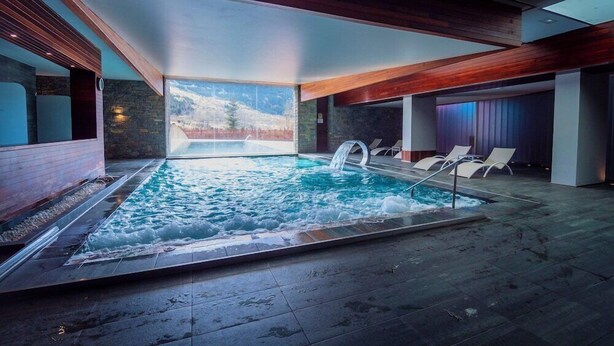 Une piscine intérieure agrémentée d’une cascade, entourée de chaises longues et d’un mur en pierre.