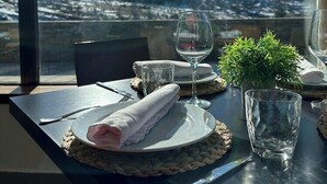 Une table dressée pour deux personnes, avec vue sur des montagnes enneigées par la fenêtre.