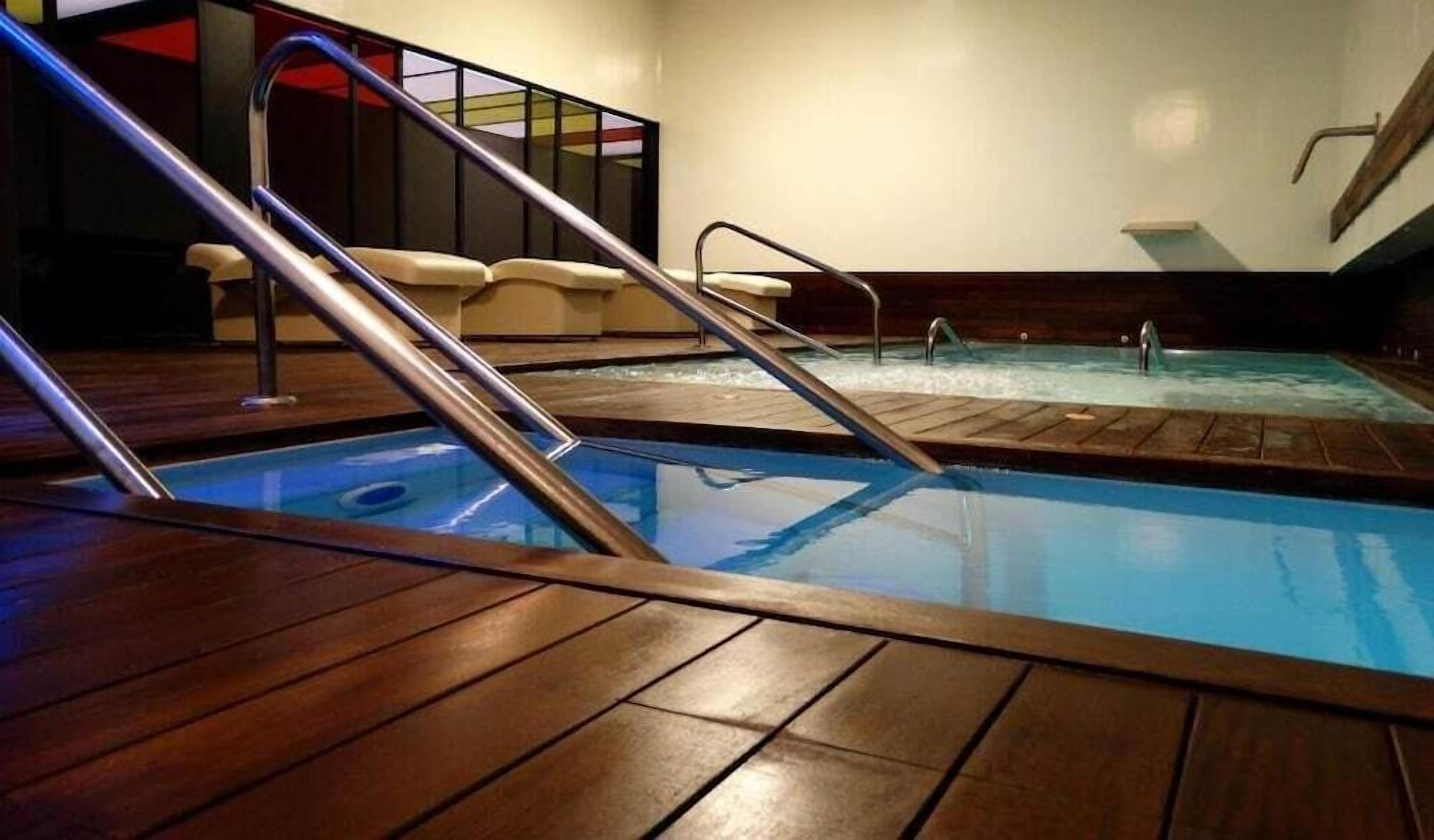 A pool area with wooden decking, a hot tub, and a staircase leading to a seating area.