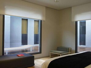 Una habitación de hotel moderna con ventanas amplias, una cama, una mesita y un banco.