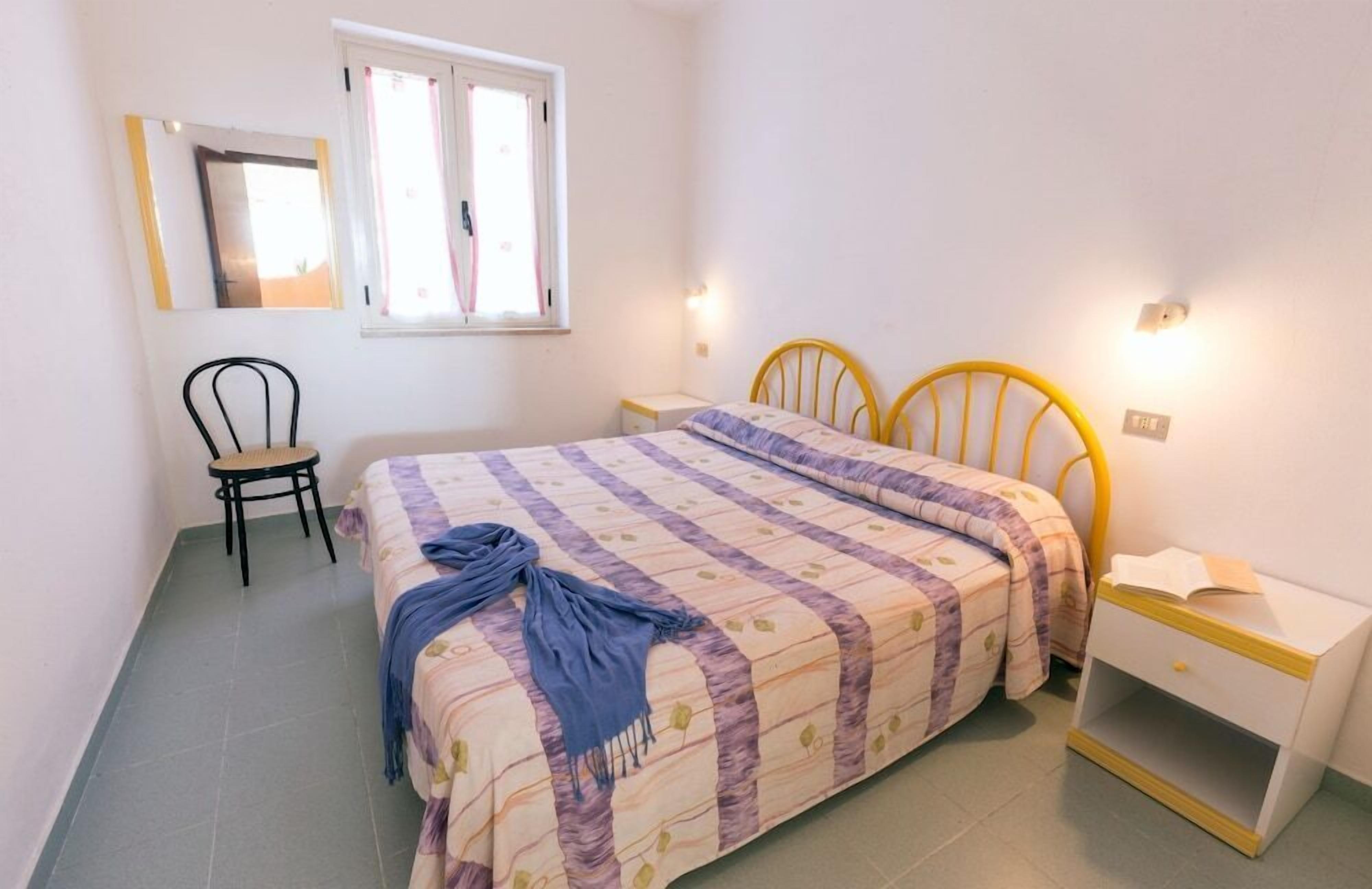 A bedroom with a bed, bedside table, chair, and a window.