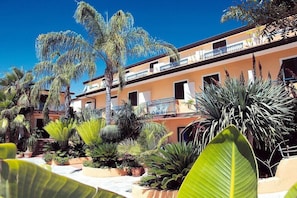 A multi-story building with balconies, surrounded by various tropical plants. - Residence Esmeraldo (Ricadi)