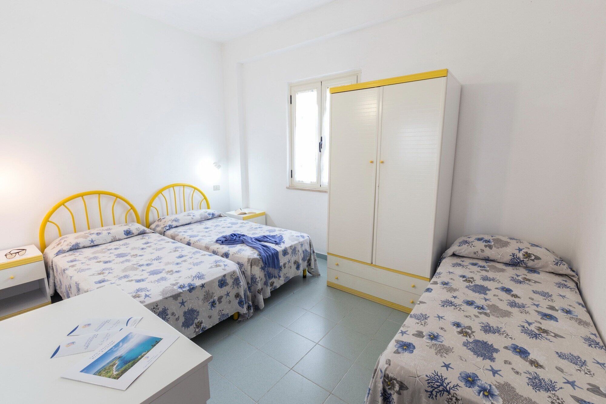 A dormitory room with two single beds, a wardrobe, a small table, and a window.