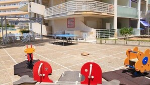 Draußen stehende Trainingsgeräte, ein überdachter Sitzbereich und ein Gebäude mit mehreren Balkonen.