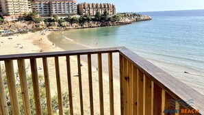 Ein Strand mit einer Holzterrasse im Vordergrund, einem Sandufer und einem Gebäudekomplex im Hintergrund.