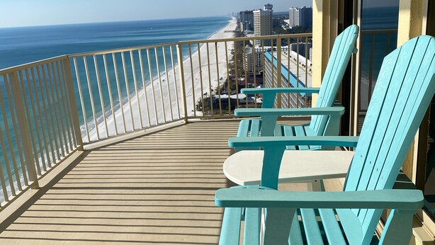 Un balcon offrant une vue sur la plage et l’océan, avec des chaises et une table de couleur turquoise.