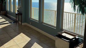 Une pièce spacieuse avec de grandes fenêtres donnant sur une plage, un sol carrelé et une plante en pot.