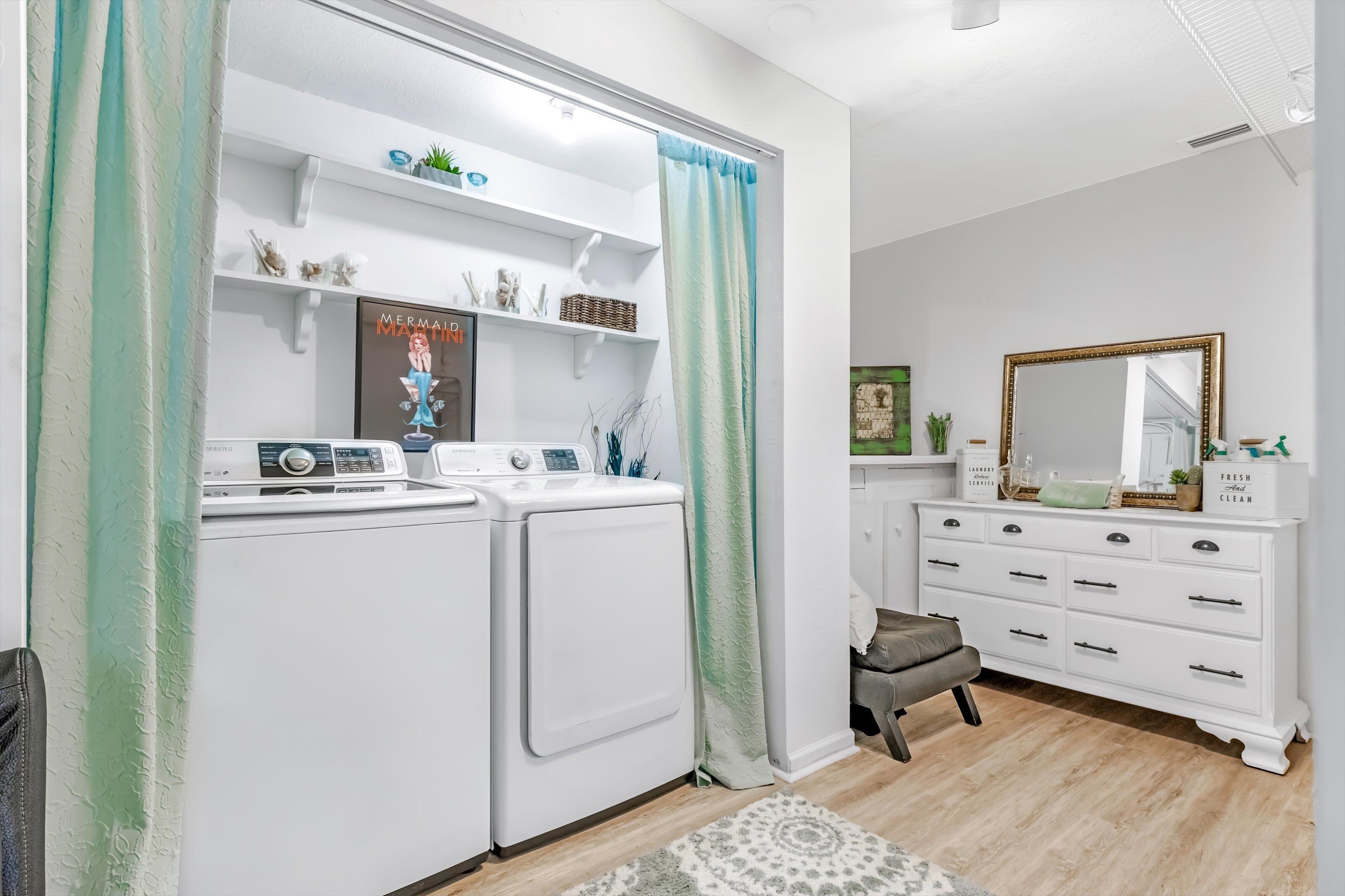 A laundry room with two washing machines, a drying rack, and a shelf with decorative items.