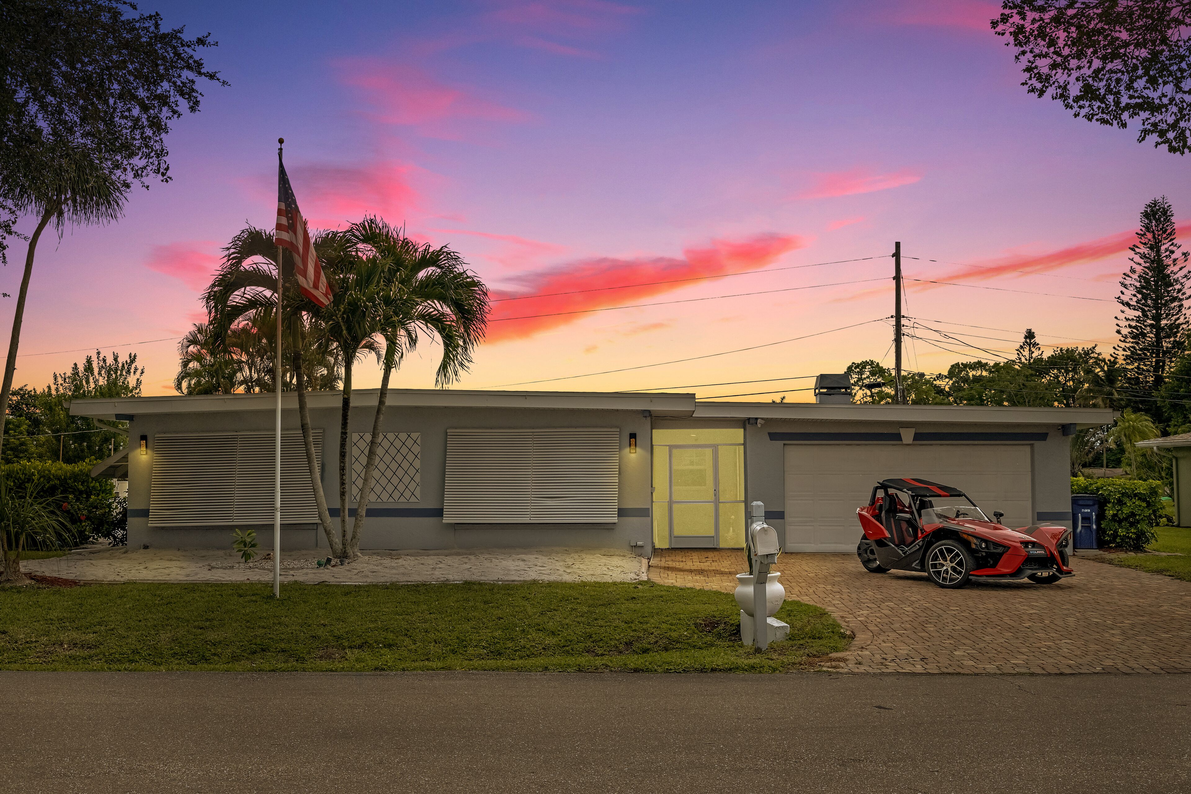 Et moderne hus med garage, en rød sportsvogn og et amerikansk flag.