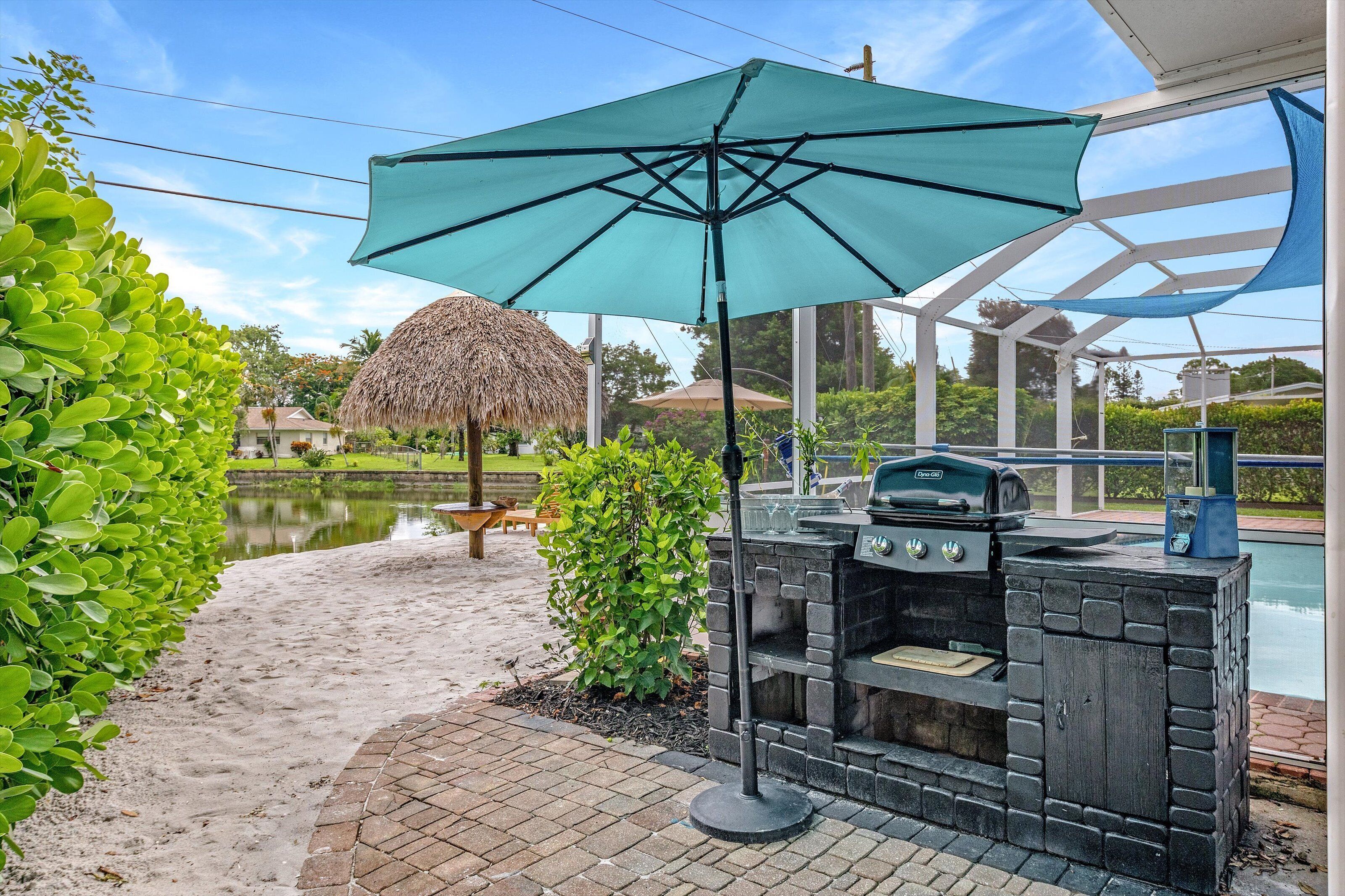 Une terrasse extérieure avec un barbecue, un parasol en chaume et une vue sur une piscine.