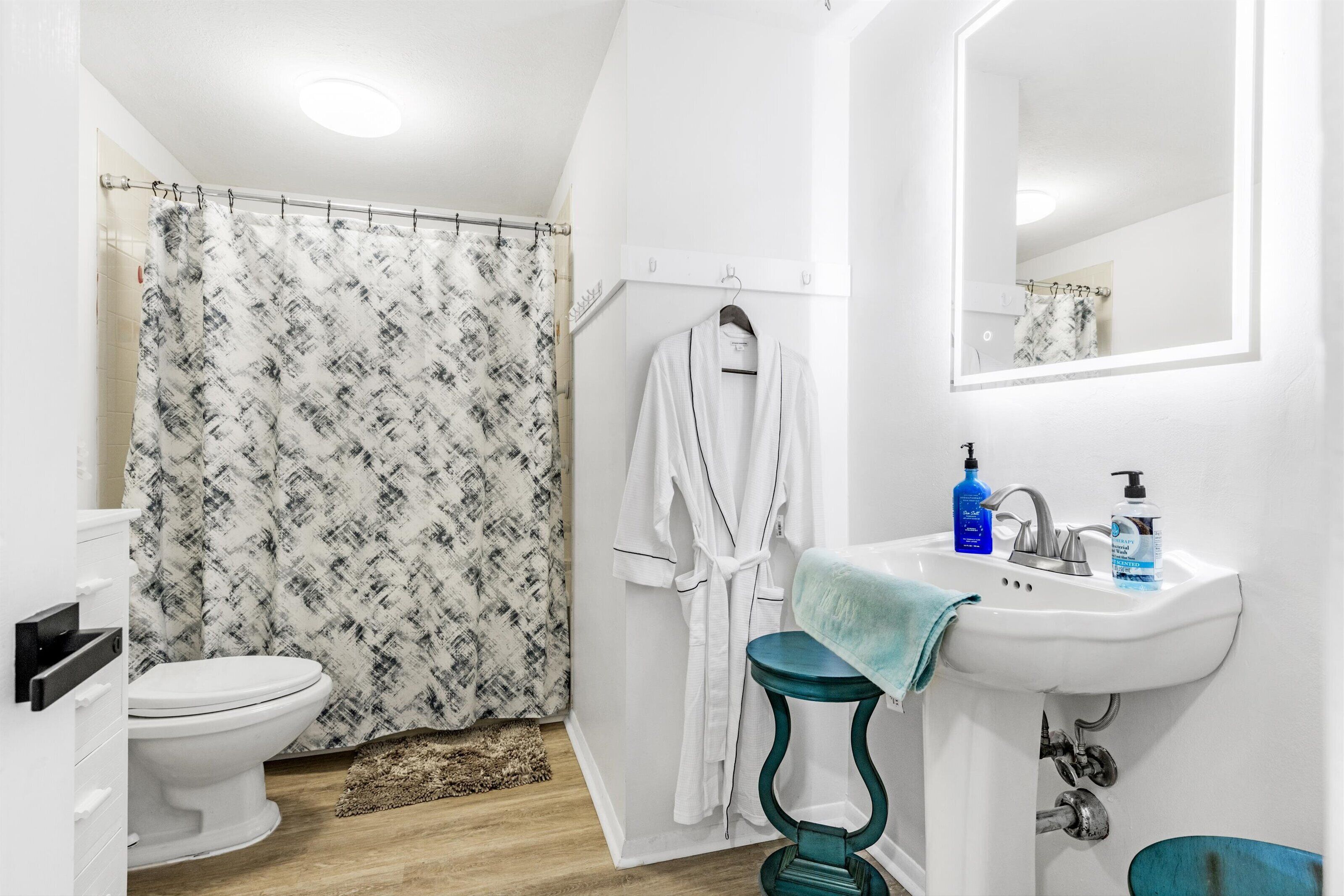 A bathroom with a toilet, shower curtain, robe, sink, and mirror.