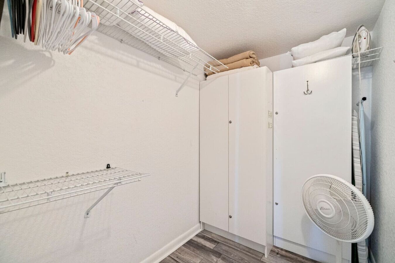 Un dressing accessible sans porte, avec un ventilateur blanc, un étendoir et une serviette pliée posée sur le dessus d’une armoire.