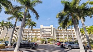 Un hotel con entrada principal, varios pisos y un estacionamiento lleno de coches.