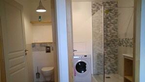Baño con inodoro, lavadora y ducha.