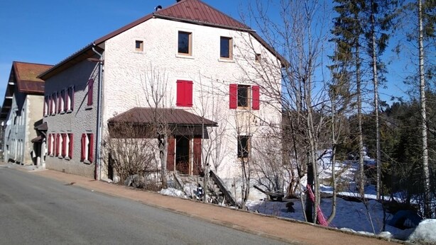 Un edificio de dos pisos con techo rojo y paredes blancas, que cuenta con un pequeño porche y una escalera que conduce a la entrada.