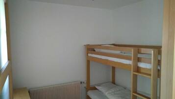 Ein kleines Zimmer mit einem einzelnen Stockbett, einem Heizkörper und einem Fenster.