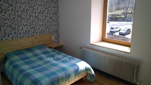Un dormitorio con cama, ventana que da a coches aparcados, radiador y pared con diseño geométrico.