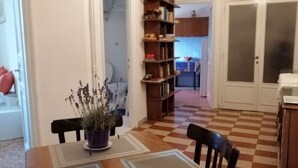 Een eethoek met een geruit vloerkleed, een tafel met een bloevas en een boekenkast.