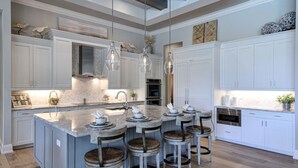 Une cuisine moderne dotée d’un îlot central, de tabourets de bar, de luminaires suspendus et de meubles de rangement blancs.