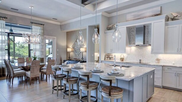 Une cuisine moderne dotée d’un grand îlot central, de tabourets de bar, de luminaires suspendus et d’éléments de rangement blancs.