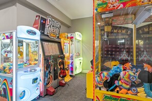 A row of arcade games including Guitar Hero and Pac-Man, with plush toys displayed in the window.