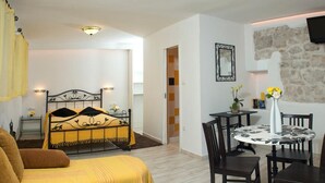 Una habitación con cama, una mesa de comedor con sillas, un televisor montado en una pared de piedra y una mesita con un jarrón de flores.