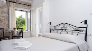 Een netjes opgemaakt bed met hoofdeinde, een tafel met stoelen en een raam met gordijnen.