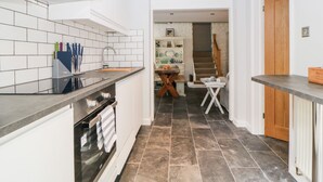 A modern kitchen with white cabinets, a black countertop, and a tiled backsplash. There is a wooden door and a staircase leading to another room. - The Old Dairy (Torpoint)