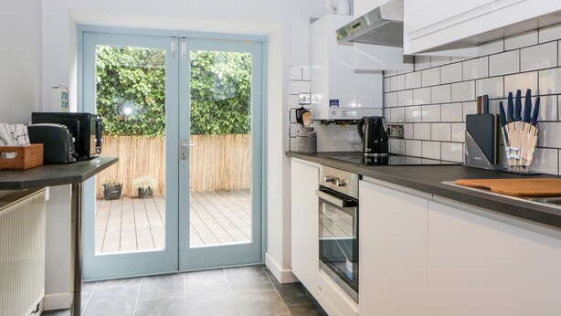 A modern kitchen with a sliding glass door leading to an outdoor area, white cabinets, a black coffee maker, and a knife block on the countertop. - The Old Dairy (Torpoint)