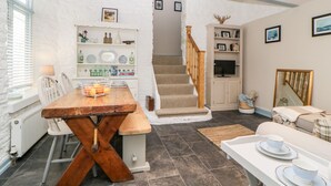 A modern kitchen with a wooden dining table, white chairs, and a staircase leading to a loft bedroom. - The Old Dairy (Torpoint)