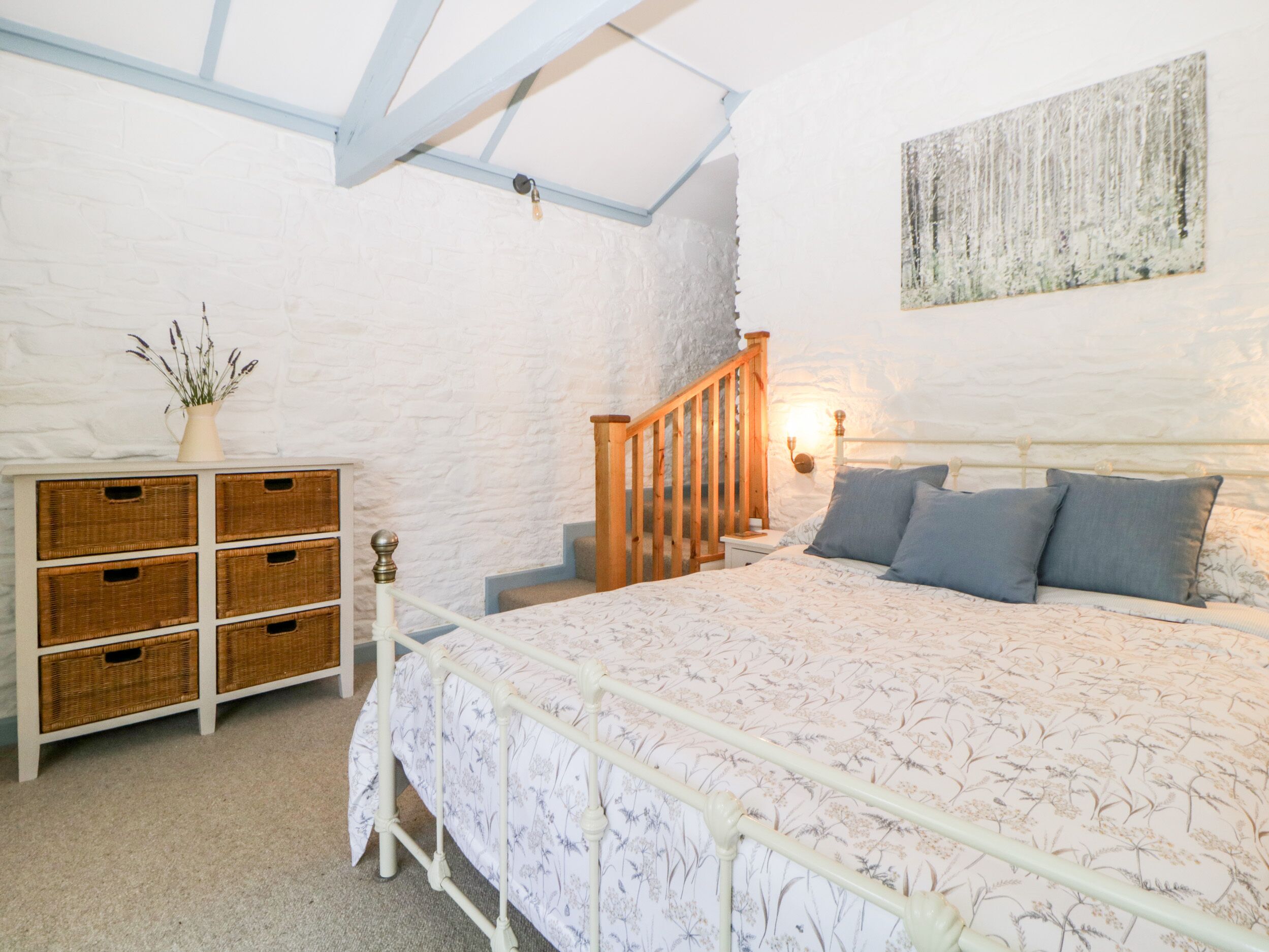 Een slaapkamer met een bed, nachtkastje, dressoir met manden, een houten trap en een wandlamp.
