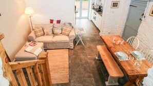A cozy room with a sofa, a wooden table set for dining, and a bench. - The Old Dairy (Torpoint)