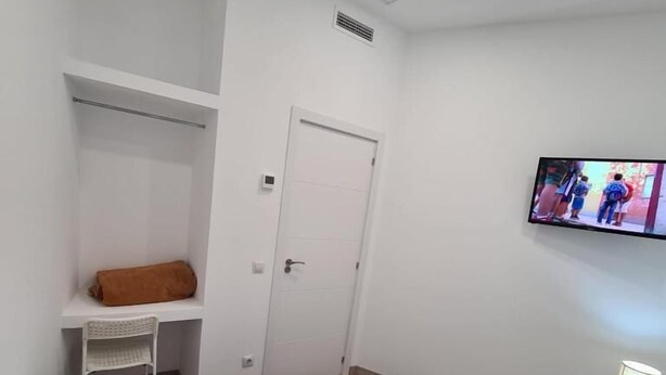 A hotel room with a bed, a TV mounted on the wall, a desk with a chair, and a wooden nightstand with a lamp. - Hostal Las Fronteras (Torrejón de Ardoz)