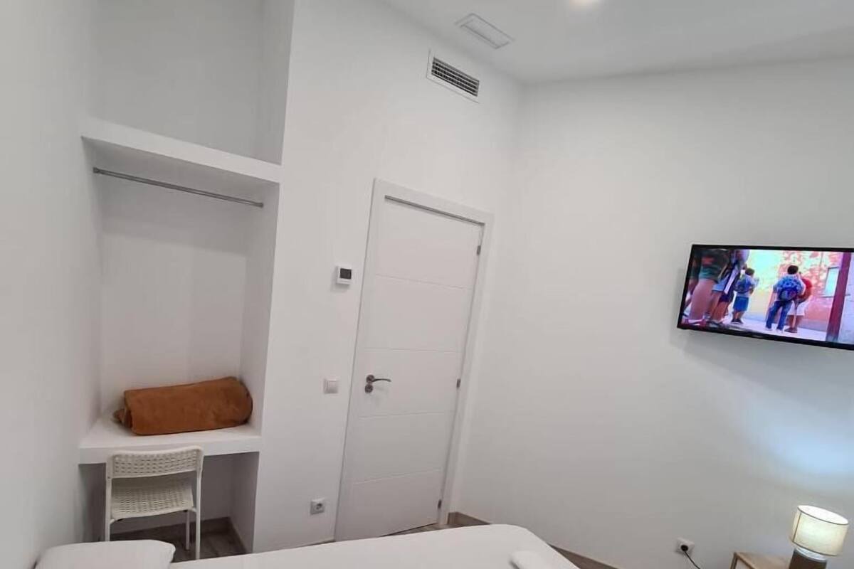 A hotel room with a bed, a TV mounted on the wall, a desk with a chair, and a door.