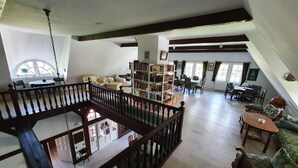 En rummelig loftsuite med højt til loftet, træbjælker, mezzanineniveau med balkon og et stort åbent opholdsområde med spisebord og stole.