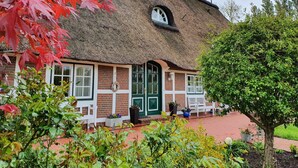 Et traditionelt bindingsværkshus med stråtækt tag, en murstensfacade, en grøn dør og en hvid bænk foran.