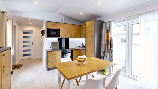 Een moderne keuken met houten kastjes, een magnetron en een eethoek met een houten tafel en witte stoelen.