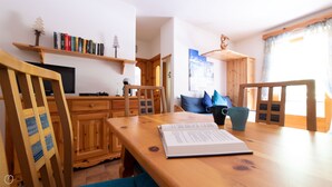 Une table de salle à manger en bois, avec un ordinateur portable et un livre, une tasse bleue et une chaise en bois avec un coussin bleu.