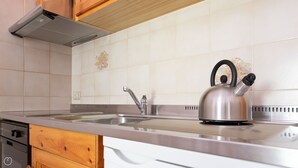 Une cuisine équipée d’une bouilloire en acier inoxydable, d’un évier à deux bacs, de meubles en bois et d’un dosseret carrelé.