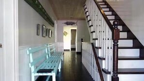 Un couloir avec un banc en bois, un escalier doté d’une rampe en bois et un mur orné de tableaux encadrés.