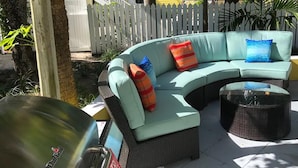 Un canapé bleu clair aux lignes courbes, doté de trois coussins, un pouf en osier et une grille métallique, le tout installé dans un espace extérieur ensoleillé.